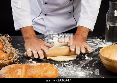 Close up of unrecognizable baker rolling batter while baking traditional bread against black background, copy space Stock Photo