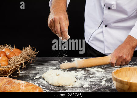 Closeup of unrecognizable baker sprinkling flour on puffy batter while making traditional bread against black background, copy space Stock Photo