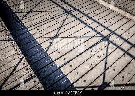 a weathered wooden bridge or decking with the shadow of the railing creating a constrasting pattern on the wood. Stock Photo