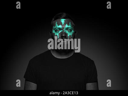 Discover what's inside you. Close up portrait of young man isolated on black studio background. Bright neon light on the face. Halloween, scary look theme, october holidays, horror concept. Stock Photo