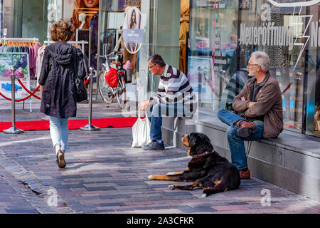 People sitting on a shop front window ledge on Kröpeliner street a busy shopping area in Rostock, Germany. Stock Photo
