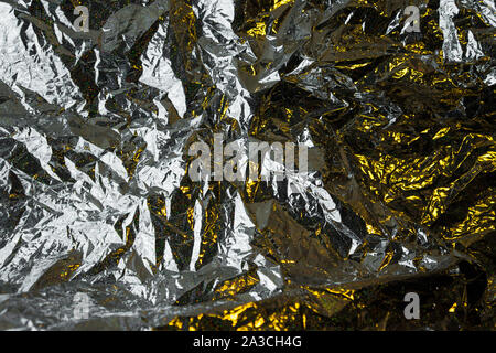 Creative photo background of silver crumpled foil with yellow highlights and shadows Stock Photo