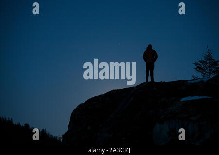 A man stands on a rock and watches a super moon rise on a spring night. Stock Photo