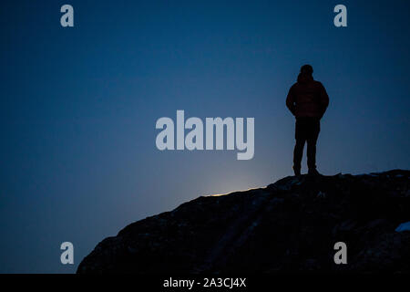 A man stands on a rock and watches a super moon rise on a spring night. Stock Photo