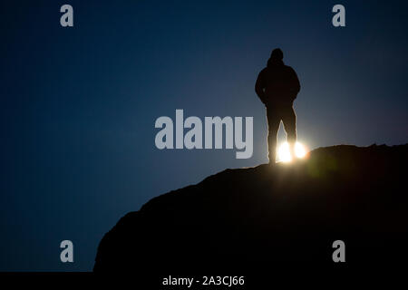 A man stands on a rock and watches a super moon rise on a spring night. Stock Photo