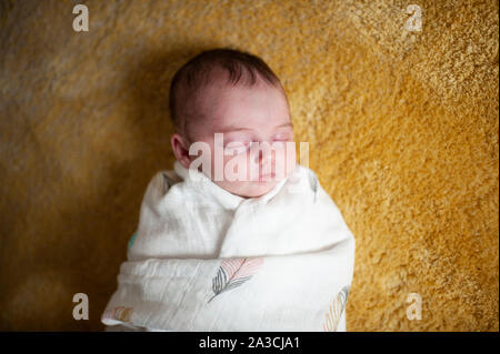 Newborn baby girl wrapped up in blanket sleeping at home on yellow rug Stock Photo