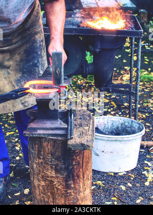 Skilled smith man striking a red hot horseshoe on the anvil. Traditional plastic deformation of molten metal. Stock Photo