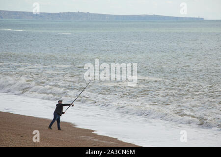 An angler casting out on Chesil beach in October the day after a storm when  the wind has dropped. Fishing after a storm can be productive as fish such  Stock Photo 