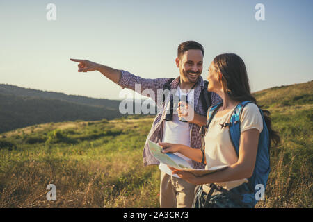 Happy couple is hiking in mountain. They are looking at map. Stock Photo