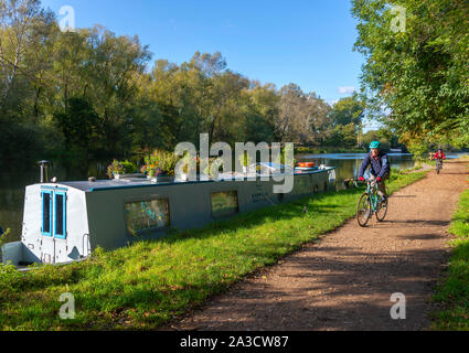 Men cycling along the Thames Path passing a narrow boat on an autumn afternoon alongside the River Thames at Sonning-on-Thames, Berkshire, England, UK Stock Photo