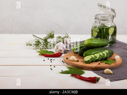 Fermented cucumbers in a glass jar, cucumbers lie on a wooden board, hot red pepper, garlic, dill, gray napkin on a wooden background. Horizontally Stock Photo