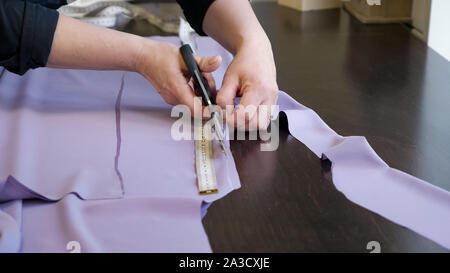 Cutting and sewing products in tailoring business. Tailor woman cutting fabric using large scissors following chalk markings of pattern, closeup hands. Dressmaker creating new clothes. Stock Photo