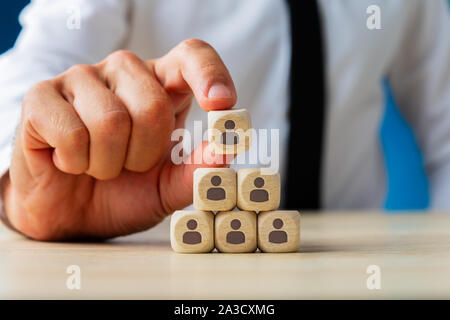 Business executive stacking wooden dices  with people icons on them in a pyramid shape in a conceptual image. Stock Photo