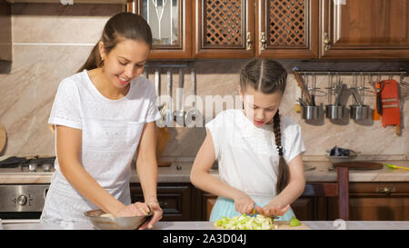 Portrait of mother and daughter are cooking apple pie together in the kitchen, mom is kneading a dough and her teen daughter is cutting apple. Stock Photo