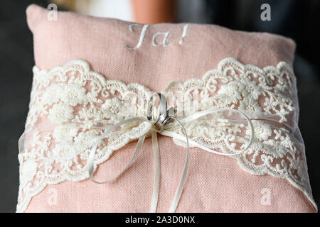 Close-up view of golden wedding rings on decorative pink ring pillow. Stock Photo