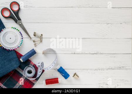 Sewing accessories, Jeans and plaid fabric with sewing threads,needle, pins, scissors, buttons and sewing centimeter on a white wooden background. top Stock Photo