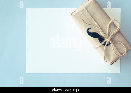 Father's day. White card and Gift package wrapped with paper and rope on light blue background. Copyspace Stock Photo