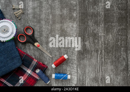 Sewing accessories, Jeans and plaid fabric on a dark wooden background. Fabric, sewing threads, needle, pins and scissors. top view, flatlay Stock Photo