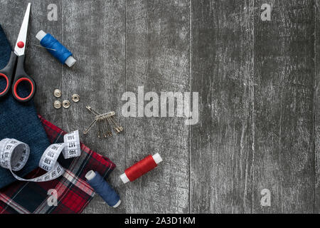 Sewing accessories, Jeans and plaid fabric on a dark wooden background. Fabric, sewing threads, needle, pins, scissors, buttons and sewing centimeter Stock Photo