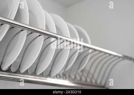 Dish drying metal rack with big nice white clean plates. Traditional comfortable kitchen. Open white dish draining closet with wet dishes of glass and Stock Photo