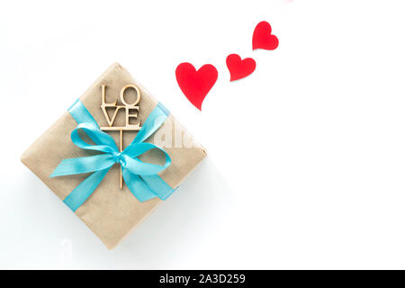 Gift box wrapped in brown paper with light blue ribbon and red hearts on white background. Top view. Copyspace Stock Photo