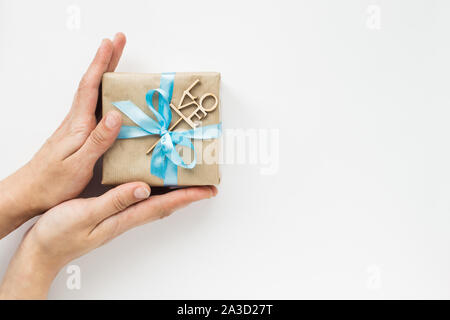Gift box wrapped in brown paper with blue ribbon in womans hands on white background. Top view. Copyspace Stock Photo