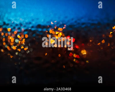 Night window with raindrops and street light of lanterns. Wet glass with multi-colored shiny drops. Blurred photo Stock Photo