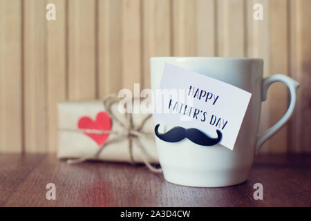 Fathers day. Greeting Message, Cup with funny mustache over wooden board. Stock Photo