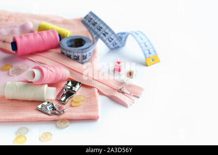 Sewing accessories and fabric on a white background. Pink fabric, sewing threads, needle, buttons and sewing centimeter. Stock Photo