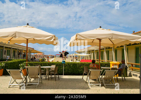 A middle-aged couple sitting under a sun umbrella in the patio of a beach with rows of huts in a sunny summer day, Viareggio, Versilia, Tuscany, Italy Stock Photo