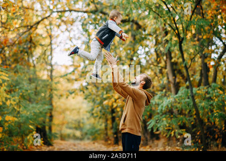 Father plays with his son and throws him up while walking in the autumn forest. Stock Photo