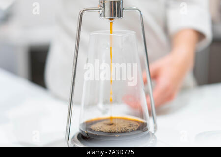 process of preparation black coffee in chemex pour over coffee maker in bright modern cafe. Alternative ways of brewing coffee. Stock Photo