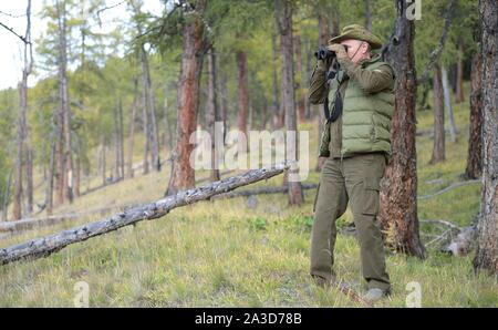 Siberia, Russia. 06 October, 2019. Russian President Vladimir Putin looks through a pair of binoculars while hiking up a mountain in the Siberian taiga forest near the Mongolian border during a birthday break October 6, 2019 in Southern Siberia, Russia. Putin turns 67-years-old on October 7th.  Credit: Alexei Druzhinin/Kremlin Pool/Alamy Live News Stock Photo