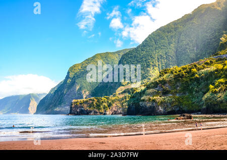 Beautiful sandy beach in Seixal, Madeira Island, Portugal. Green hills covered by tropical forest in the background. People on the beach. Summer vacation destination. Portuguese landscape. Stock Photo
