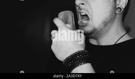 Man screaming on the microphone. Singing heavy metal. Close-up on a man wearing black, holding a studio microphone. Stock Photo