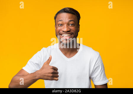 Afro Guy Gesturing Thumbs-Up Smiling At Camera, Yellow Background Stock Photo