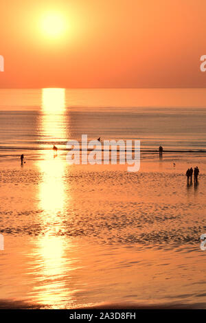 Plage de Ault Onival au crépuscule, soleil couchant, à l'horizon sur une mer d'huile à marée basse. promeneurs et pêcheurs sur la plage. Stock Photo