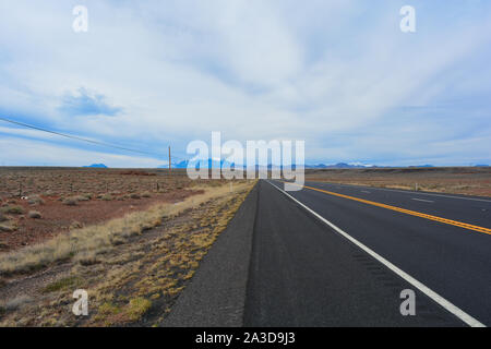 Straight road running in the desert with a panoramic mountain view. Silent afternoon on a peaceful highway with remote mountain peaks. Beautiful USA Stock Photo