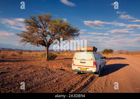 4x4 rental car equipped with a roof tent driving on a dirt road in Namibia Stock Photo