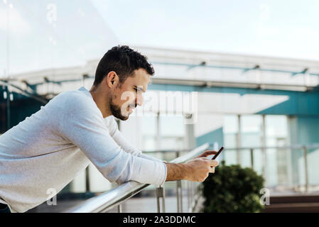 Young man leaning on railing while using mobile phone Stock Photo