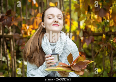 The girl relaxes and drinks coffee from a thermos. Autumn in the park. Life style concept, autumn, relax and reading. Stock Photo