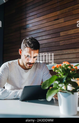 Stylish young man sitting on couch in a cafe using tablet Stock Photo