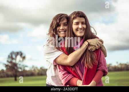 two female friends hug and laugh outdoors on green farm land Stock Photo