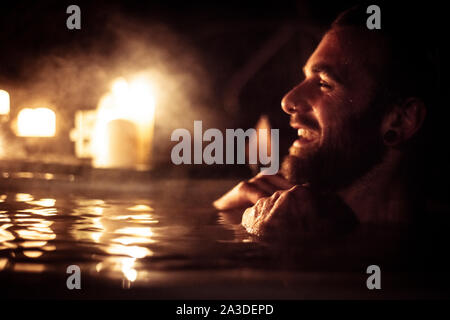 Man in out door hot tub smiles with candle light and steam Stock Photo