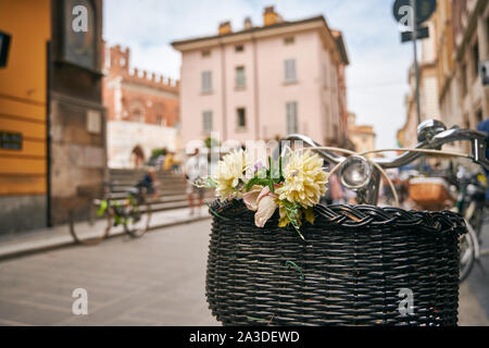 Selective focus of vintage bicycle with wicker basket full of flowers on medieval street in Tuscany Stock Photo