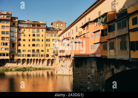 Apartment buildings with shabby balconies located on stone bridge over river on cloudless sunny day in aged city in Tuscany, Italy Stock Photo