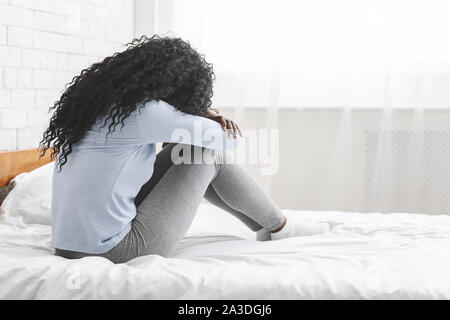Back view of lonely young woman sitting on bed Stock Photo