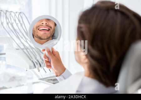 Satisfied patient checking smile at mirror in dental clinic Stock Photo