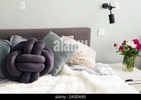 Bed with a lot of decorative pillows and peonies on the night stand. Stock Photo