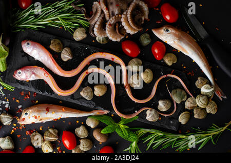 Fresh mixed sea fish, octopus, tomatoes and rosemary on a grill pan on dark bacground. Meditteranean food concept. Top view